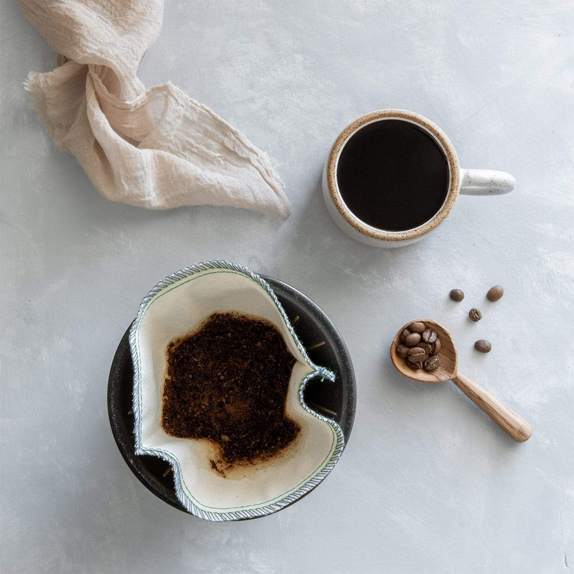 Organic coffee filter with grounds, bamboo spoon with coffee beans, and coffee cup